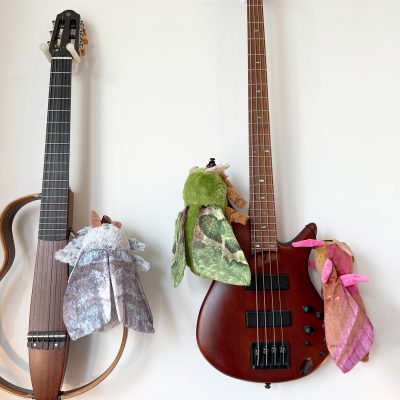 Three plush moth toys in pastel colors resting on acoustic and bass guitars – EdenWave