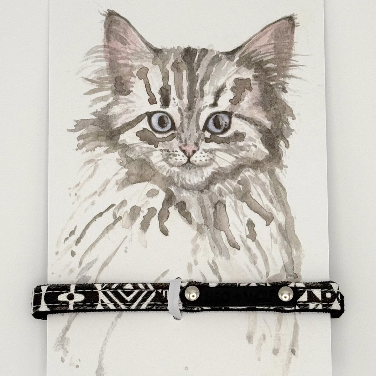 HW-CAT-0001_Strech Cat Collar_Card copy Hiro + Wolf Bow Wow Haus Stretch Cat Collar in black and white geometric print with safety bell, displayed on a brand card featuring a hand-drawn cat illustration.