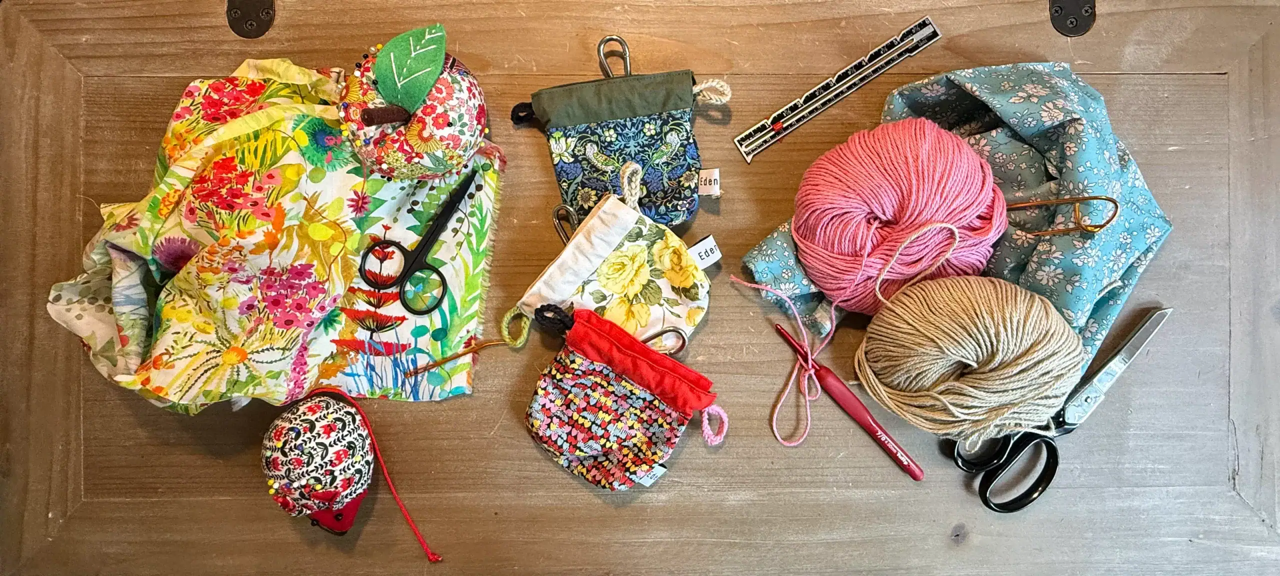 EDENWAVE original handmade poop bag holders in three fabric patterns on a maker's table with yarn and crochet tools